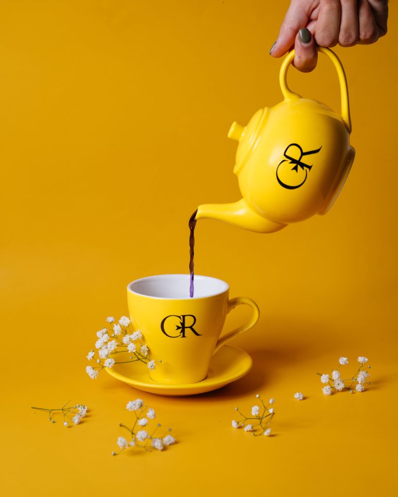 Yellow teapot pouring into cup, floral, bright background.