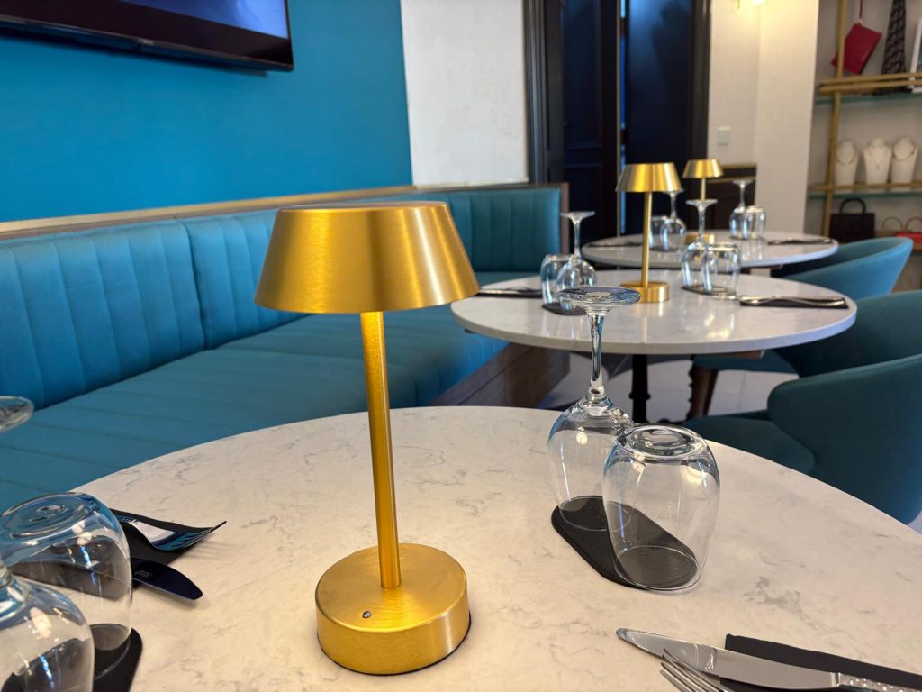 Marble-top café tables, gold lamps, wine glasses, teal seating.