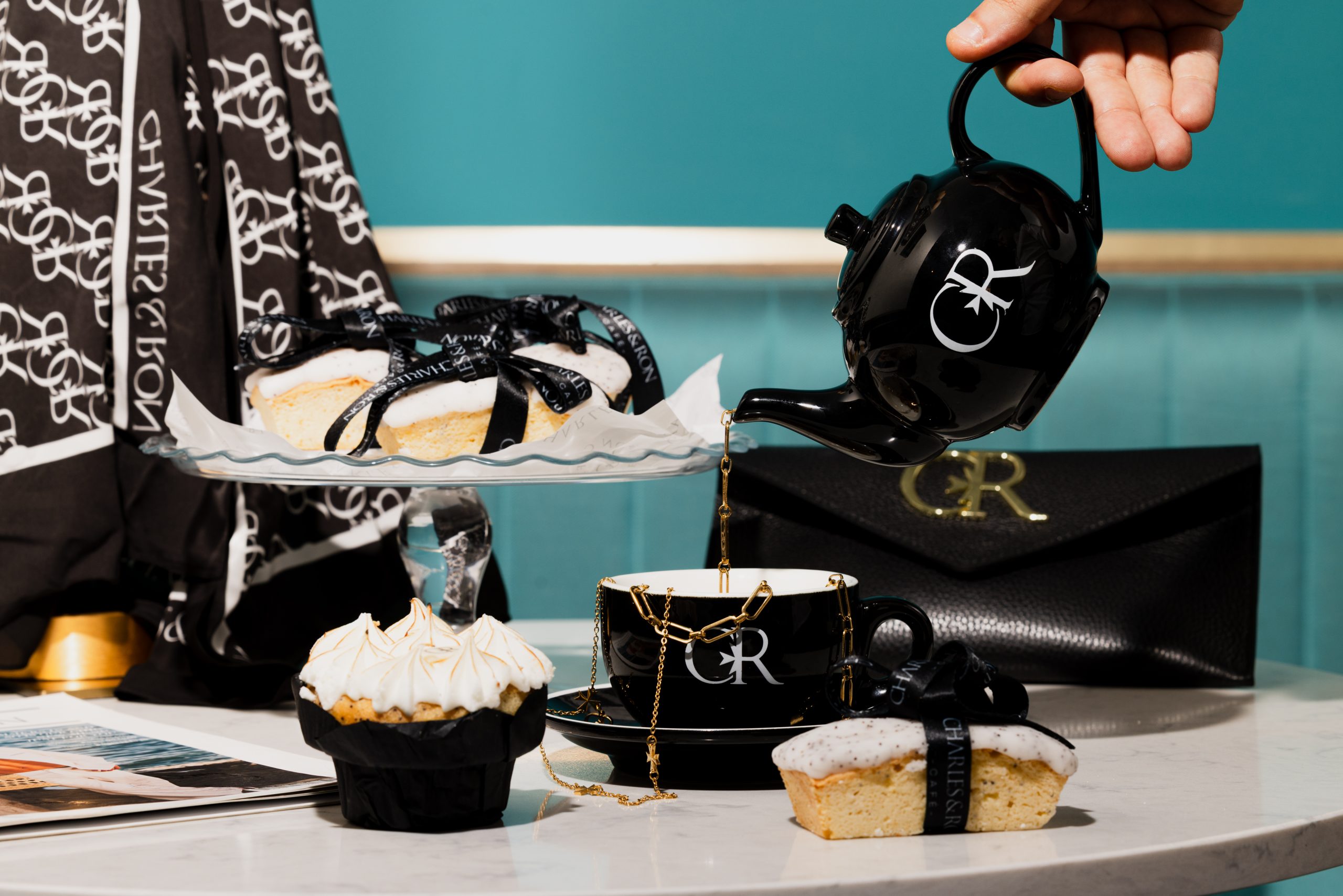 Black and gold CR-branded afternoon tea set: teapot, cup, cakes, purse, fashion accessories, hand pouring